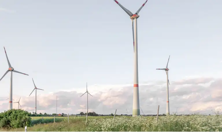 Windräder stehen in der Abenddämmerung in der hessischen Landschaft mit Feldern.