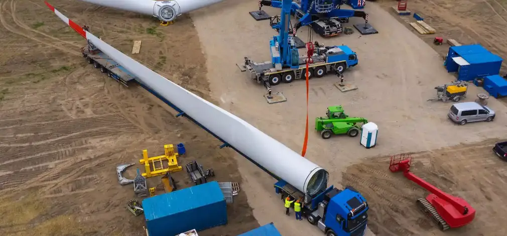 Luftaufnahme einer Windrad-Baustelle im Aufbau mit Baufahrzeugen und Bauteilen.