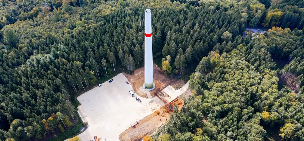 Luftaufnahme eines im Bau befindlichen Windradturms im dichten Wald.