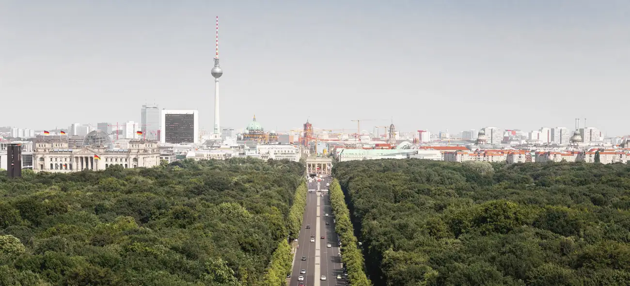 Blick auf den Berliner Fernsehturm, Stadt und das Brandenburger Tor über Baumwipfeln im Sonnenuntergang.