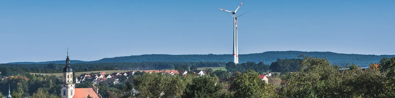 Kirche am Ortsrand mit Windrädern im Hintergrund.