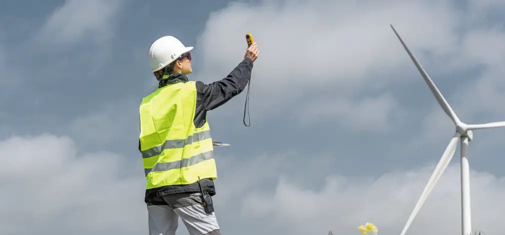 Für eine Standortbewertung sind Messungen der Windbedingungen unabdingbar. Präzise Daten dienen als Grundlage für erfolgreich umgesetzte Windkraftprojekte. Techniker in Warnweste misst mit einem Messgerät die Windhöffigkeit bei einer Windenergieanlage.