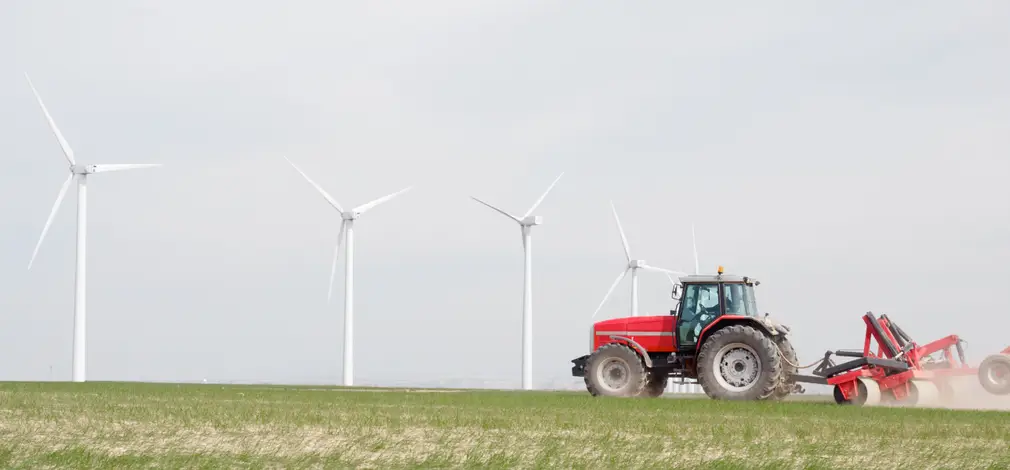 Roter Traktor pflügt auf einem Acker, im Hintergrund mehrere Windräder.
