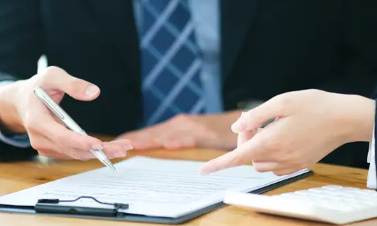 Windkraft-Pachtvertrag: So gestalten und verhandeln Sie erfolgreich Zwei Personen sitzen am Tisch, eine Person hält einen Stift über einem Vertrag zum Windkraft-Pachtvertrag.