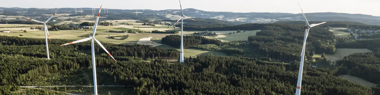 Luftaufnahme eines Windparks mit mehreren Windrädern über Wald- und Agrarlandschaft.