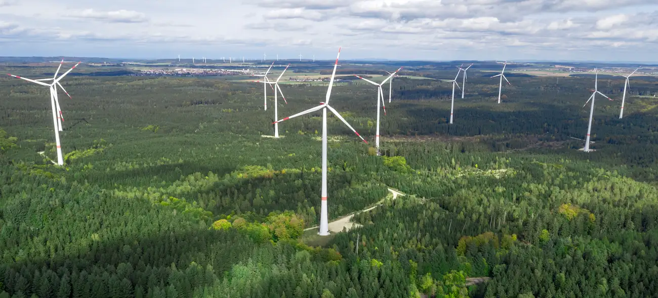 Argumente gegen Windkraftanlagen im Wald – zwischen Mythen und Fakten Windpark in einer bewaldeten Landschaft, Windräder ragen über die Baumwipfel.