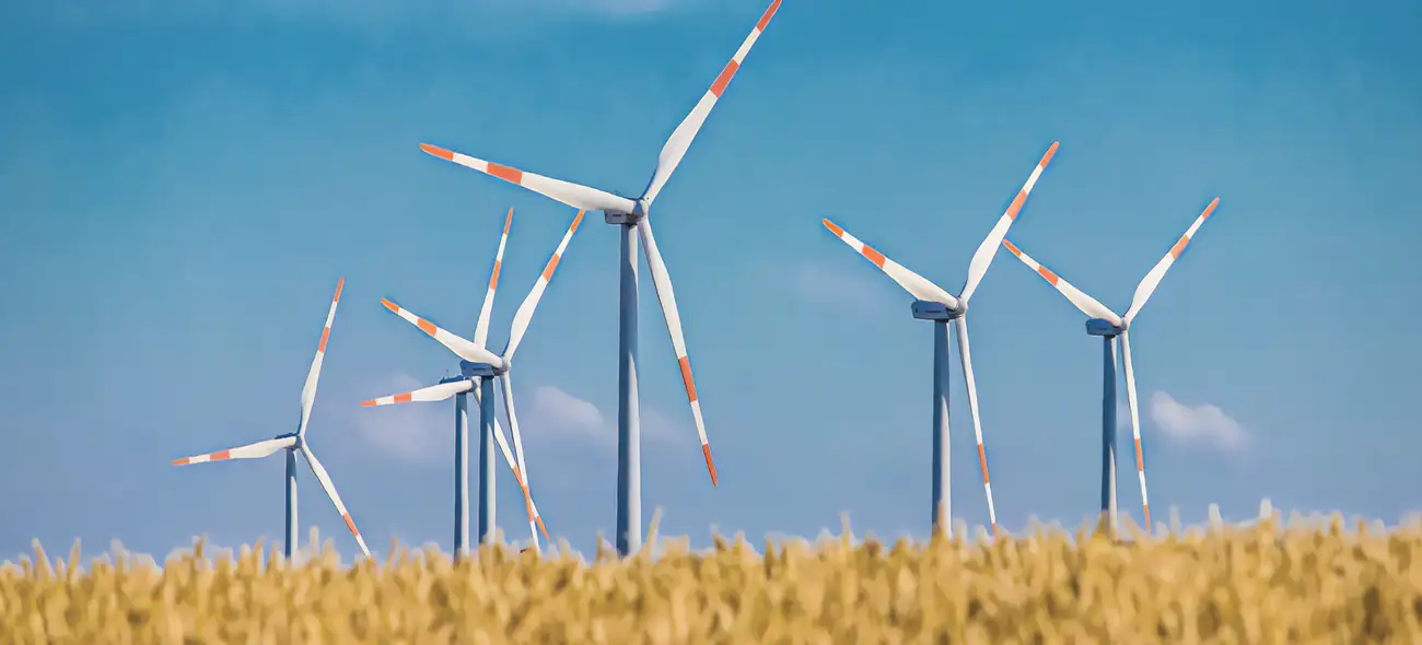 Flächenpooling bei Windkraftprojekten: Mit gebündelten Flächen den Ausbau vorantreiben Windräder aus Flächenpooling-Projekt für Windkraftanlagen auf einem Feld unter blauem Himmel.
