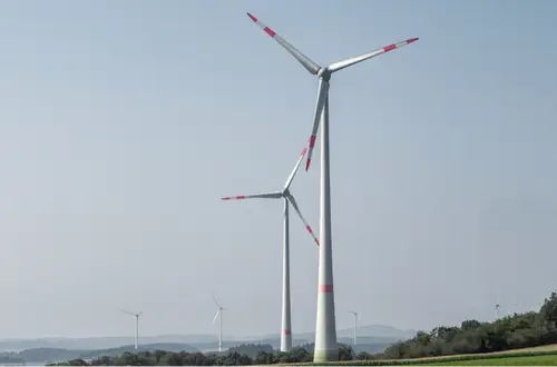Mehrere Windräder auf grüner Landschaft unter blauem Himmel in Nordrhein-Westfalen.