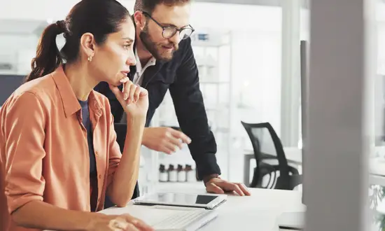 Windkraftflächen erfolgreich sichern: Strategien für Projektentwickler in einem dynamischen Markt Zwei Personen betrachten im Büro Dokumente zu Windkraftflächen auf einem Monitor.